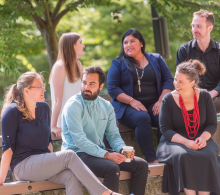 Six professionals sitting outdoors looking at one another and smiling.